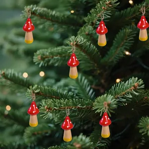 Nahaufnahme von roten Holzpilz-Anhängern, die an grünen Weihnachtsbaumzweigen hängen