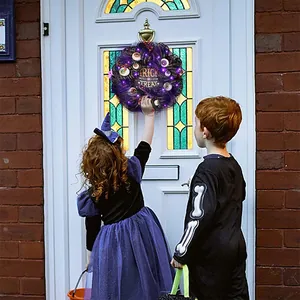 Halloween wreath with glowing eyeballs and Trick or Treat sign on a white door