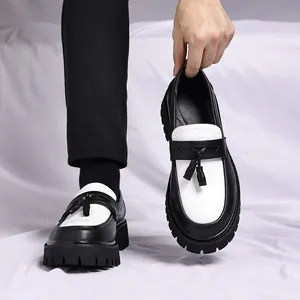 Detailansicht von schwarz-weißen klobigen Slippern mit Quasten auf weißem Grund.