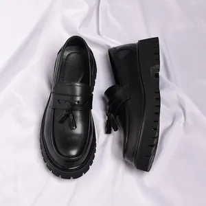 Λεπτομέρεια μαύρων ανδρικών loafers με πλατφόρμα και κλασικές φούντες σε λευκό ύφασμα.