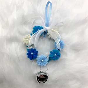 Primo piano di una ghirlanda di Natale blu in scovolini con fiocco in organza bianca e campanella.