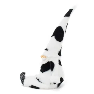 Side view of a plush cow print gnome doll sitting on a plain white background