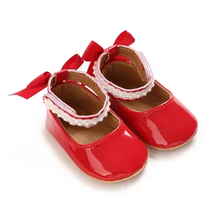 Close-up of glossy red baby girl princess shoes featuring a bow and pearl lace trim.