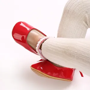 Close-up of red patent leather baby princess shoes with pearl ankle strap on feet.