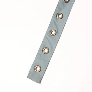 Detailed macro view of antique bronze metal eyelets on light blue denim fabric strap