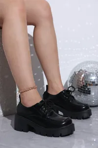 Gros plan de mocassins noirs à plateforme et talons épais portés par un modèle.