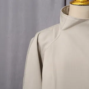 Dettaglio del colletto alto e della spalla raglan di un trench beige dal design minimalista.