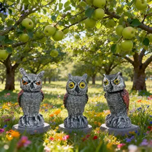 Three realistic owl bird deterrent decoys with rotating heads in a sunny apple orchard.
