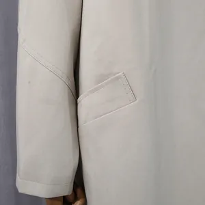 Dettaglio della tasca e della trama del tessuto twill su un trench primaverile beige.