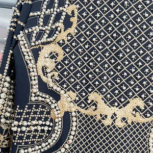 Dettaglio di un blazer con stampa barocca dorata e eleganti decorazioni in perle sintetiche.
