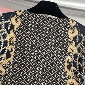 Dettaglio ravvicinato di ricamo con perle bianche e griglia dorata su blazer nero