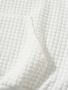 Detailreiche Makroaufnahme, die die weiche Textur des weißen Waffelstrickstoffs zeigt.