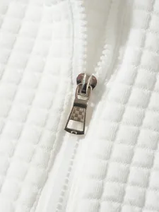 Detailaufnahme der weißen Waffelstrick-Struktur und des silbernen Metall-Reißverschlusses.