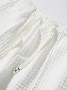 Macro detail of white waffle-textured trousers showing elastic waistband and drawstring.