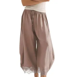 Gros plan montrant l'ourlet en dentelle complexe sur un pantalon large taupe pour femme.