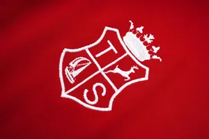Λεπτομερές κοντινό πλάνο λευκού κεντητού εμβλήματος σε κόκκινο βαμβακερό μπλουζάκι πόλο