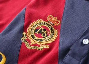 Detailed close-up of crest embroidery on a red and navy blue color-block men's polo shirt