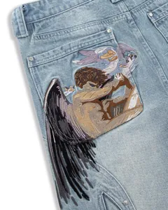 Detailed view of elaborate fallen angel embroidery on light wash denim jeans.