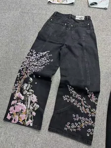 Dettaglio del ricamo con fiori di ciliegio rosa e cavaliere su jeans neri a gamba larga