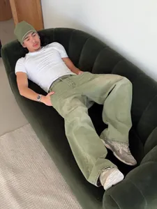 Macro detail of baggy matcha green denim jeans on a male model lounging on a green sofa.
