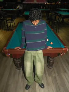 Lifestyle shot of matcha green loose-fit jeans with washed gradient in a pool hall.