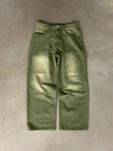 Flat lay view of matcha green washed gradient wide-leg denim jeans on a textured gray floor.