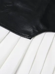 Detalle de falda plisada de talle alto con diseño de patchwork de cuero negro.