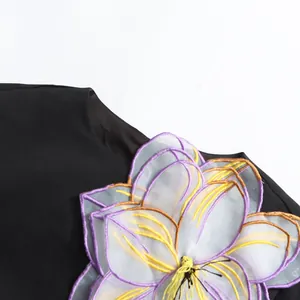 Primer plano del bordado floral en 3D de una elegante blusa negra de manga corta estilo francés.