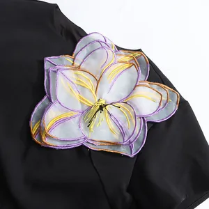 Primer plano del aplique floral en 3D con bordados morados en un elegante top negro francés