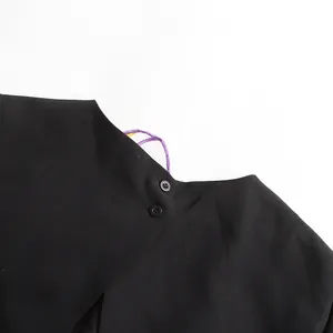Detalle de cerca de un top negro de estilo francés con botones dobles y detalle púrpura.