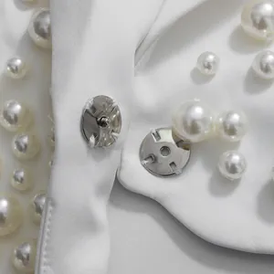 Dettaglio ravvicinato di decorazioni in perle e bottone a pressione su un capo bianco