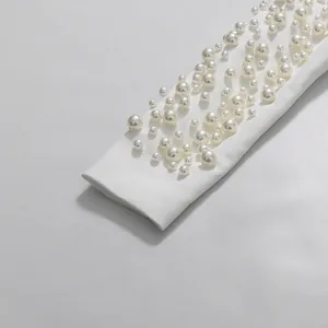 Macro dettaglio di un'elegante manica bianca ornata con perle di varie dimensioni