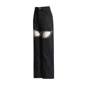 Detail of black high-waisted wide-leg jeans with rhinestone-trimmed cut-outs on thighs.