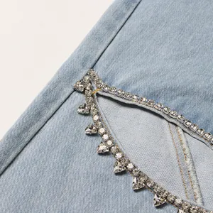 Close-up of rhinestone embellishments and hollow-out design on light blue denim jeans
