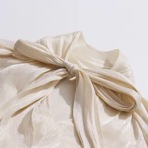 Detalle del elegante cuello con lazada de una blusa plisada beige brillante