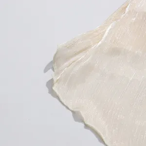 Detalle de tela brillante con textura plisada y dobladillo ondulado en blusa mujer.