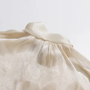 Primer plano de la tela plisada brillante y el cuello alto de una blusa beige suave