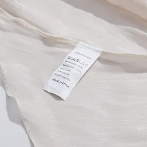 Detalle de la etiqueta de lavado de una blusa de gasa plisada blanca 100% poliéster