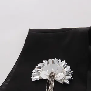 Vue détaillée d'une fleur à paillettes argentées et d'un gland métallique sur un gilet noir.