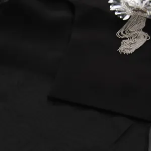 Gros plan d'un gilet noir avec fleur en paillettes 3D et détails de franges en métal
