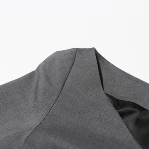 Detail van de asymmetrische halslijn en schouder op een grijze getextureerde blazer