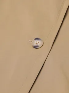 Macro detail of beige trench coat fabric with a faux horn button and fine stitching.