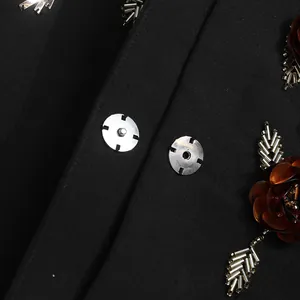Detailed macro view of metallic 3D flower applique and metal snap button on black blazer