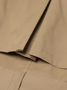 High-resolution close-up of stitching and pleated fabric detail on a khaki trench coat