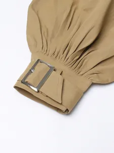 Close-up of khaki trench coat cuff featuring silver buckle and pleated detail