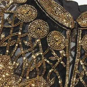 Gedetailleerde macro-opname van het complexe gouden kralenwerk op deze zwarte shrug