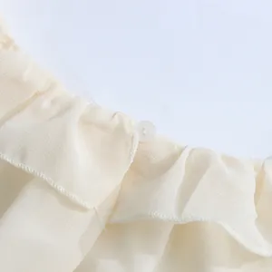 Detailopname van de gelaagde ruches en knoopsluiting op een crème chiffon shirt.