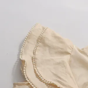 Close-up detail of beige flutter sleeve with delicate pom-pom lace trim.