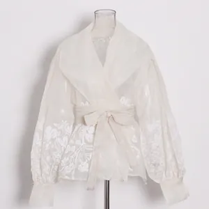 Exquisite details of a vintage white embroidered organza blouse featuring a chic waist tie.