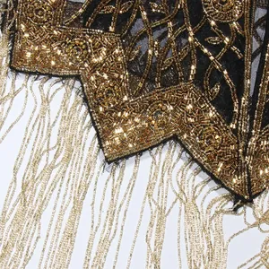 Detailopname van luxe gouden kralenborduursel en franjes aan een zwarte cape in Franse stijl